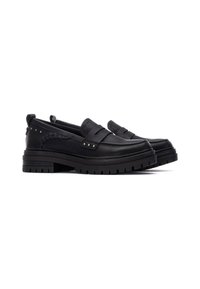 Zapatos de cuero negros tipo slip-on que presentan una suela gruesa, detalles trenzados y tachuelas metálicas en el lateral para añadir textura y estilo.