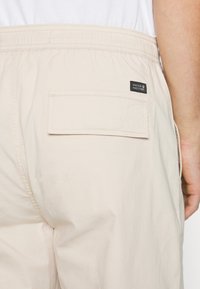 Beige shorts lavet af letvægtsstof, med en elastisk talje, en baglomme med klap og en lille sort labeldetalje.
