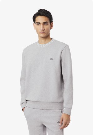 Gray sweatshirt with a crew neckline, featuring Lacoste branding along the collar and a small logo on the chest. Soft texture.