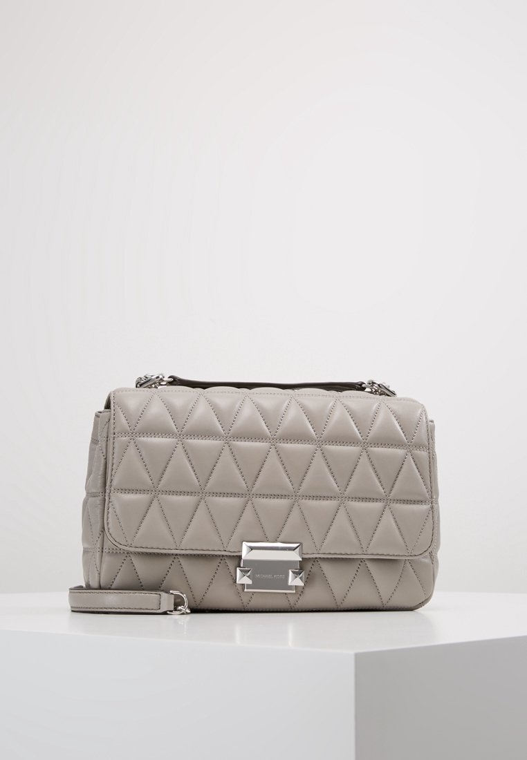 Sac à main en cuir gris matelassé avec fermoir rectangulaire argenté et sangle amovible, posé sur une surface blanche sur fond uni.