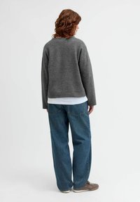 Grå stickad tröja med lös passform, ribbade ärmslut och rak nederkant, kombinerad med blåa baggy jeans och grå sneakers. Subtila texturdetaljer synliga.