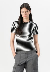 T-shirt de manga curta preto e branco às riscas com decote redondo, feito de um tecido suave, usado com calças cargo cinzentas com bolsos laterais.