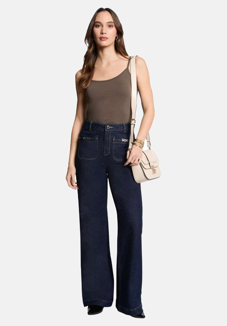 Jean évasé taille haute bleu foncé avec poches avant, associé à un haut sans manches marron et un sac bandoulière beige. Texture lisse, look décontracté.