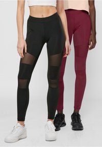 Svart og maroon leggings med mesh-paneler, tettsittende design og en glatt tekstur, parret med hvite og svarte sneakers.