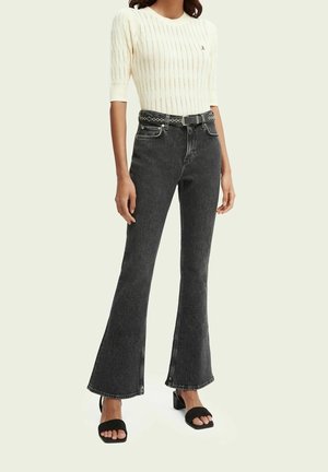 Schwarze, ausgestellte Jeans mit hoher Taille, kombiniert mit einem taillierten, cremefarbenen Rippenstrickoberteil. Merkmale sind ein strukturiertes Design und ein dezenter Gürtel.