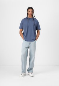 T-shirt azul de gola redonda combinado com jeans de perna reta azul claro, usado com tênis brancos. Tecido suave, ajustado de forma relaxada e design minimalista.