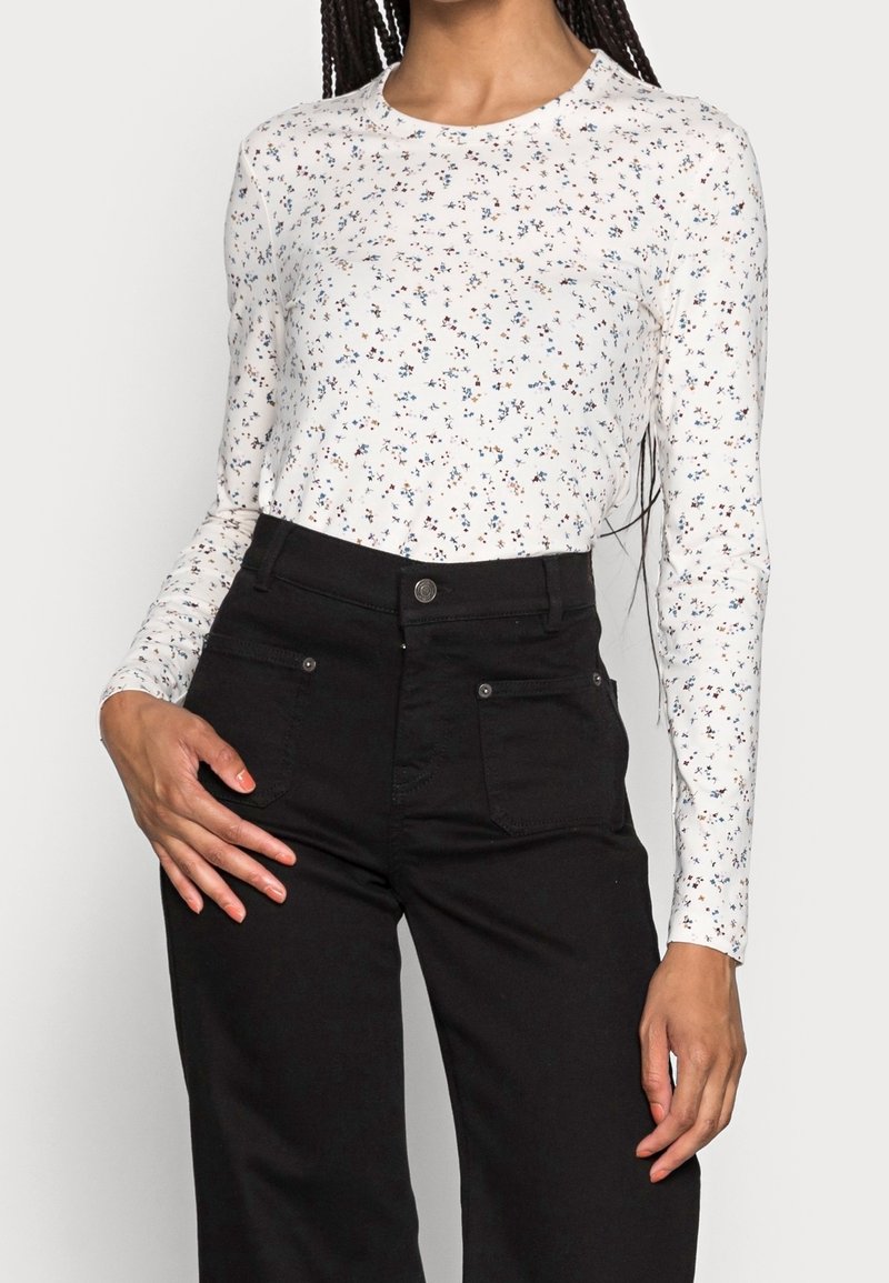 Wit shirt met lange mouwen en een bloemenpatroon in blauw en rood. Combineer met zwarte, hooggerichte broeken met steekzakken aan de voorkant. Soepele stoftextuur.