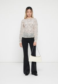 Doorschijnende lichtroze lange mouw top met zilveren pailletjes en een rafelige zoom, gecombineerd met zwarte flared broek en een crèmekleurige handtas met kettingband.