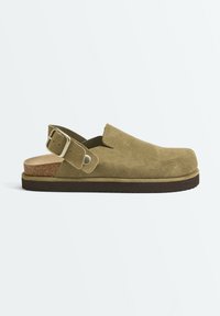 Sabot fermé en daim vert olive avec bride arrière ajustable, semelle intérieure en liège et semelle en caoutchouc foncé sur fond uni.