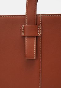 Sac fourre-tout en cuir marron avec une texture lisse, présentant une attache de poignée cousue et une structure plate.