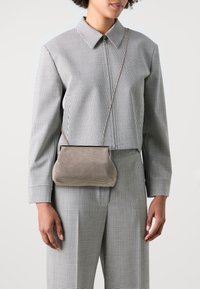 Torebka crossbody o uporządkowanym kształcie, pleciony materiał w beżowo-czarną kratę, z górną ramą i cienkim paskiem na ramię.