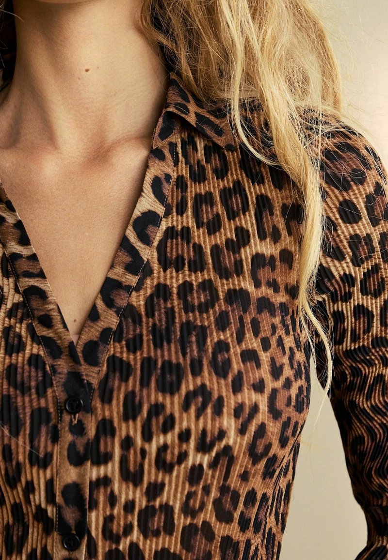 Camisa de estampado de leopardo en marrón y negro, con diseño de cuello, tejido texturizado y cierre de botones en la parte delantera.