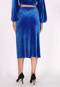 Midirock aus blauen Samt mit enganliegendem Schnitt, der einen subtilen Glanz und einen mittigen Schlitz hinten hat. Kombiniert mit schwarzen Stiletto-Absätzen.