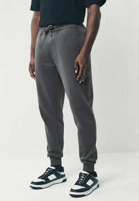 Gray sweatpants with a drawstring waistband, slim fit, ribbed cuffs, paired with black and white sneakers featuring a lace-up design.