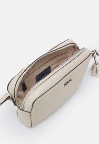 Krémová kožená taška se strukturovaným tvarem, vybavená horním zipem a vnitřní kapsou. Diskrétní embosované logo na přední straně.