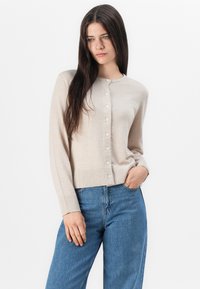 Beige cardigan med rund hals, lange ermer og knappestolpe, med ribbede detaljer på ermene og kanten.