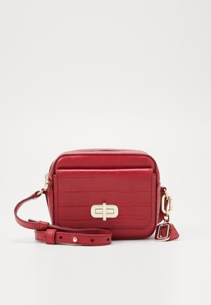 Mała czerwona torebka na ramię o fakturze krokodyla, przednia kieszeń z złotym zamkiem typu turn-lock, regulowany pasek oraz złoty ozdobny element.