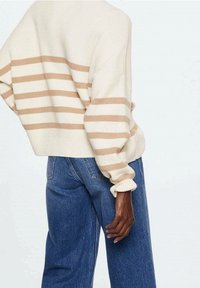 Pull en crème avec des rayures beiges, coupe ample, texture côtelée et manches ballons, associé à un jean en denim bleu taille haute.