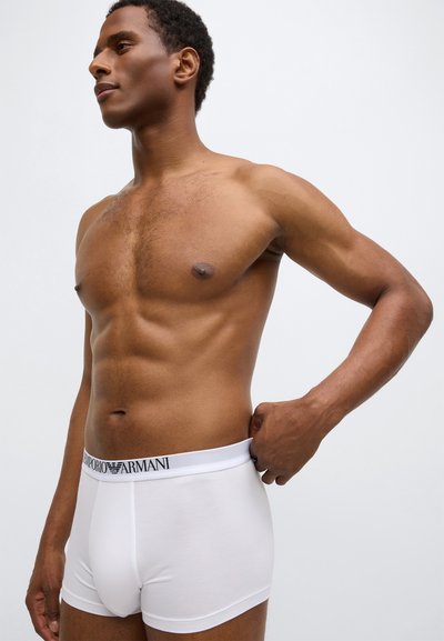 Boxer blanc avec une texture douce et une taille élastique noire avec logo, coupe ajustée, présentant un devant plat et une tenue proche du corps.
