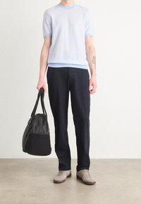 Suéter de mangas cortas azul claro con un escote en contraste, combinado con pantalones oscuros. Se incluyen zapatillas grises y un bolso negro.