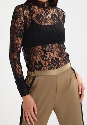 Svart spets långärmad topp med blommönster, med en hög krage och genomskinlig textur, lager över en svart camisole.