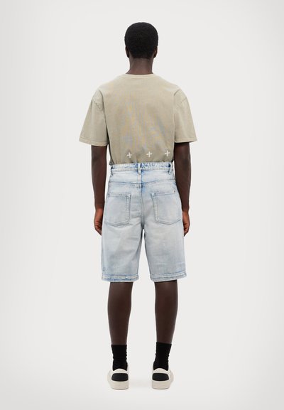 T-shirt cinza claro com um padrão geométrico, combinado com calções de ganga azul claro. Meias pretas e ténis com detalhes em branco e preto.