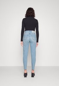 Ljusblå högmidjade jeans med en figurnära design, fem fickor och en ren baksida. Bärs med en svart långärmad topp och klumpiga klackskor.