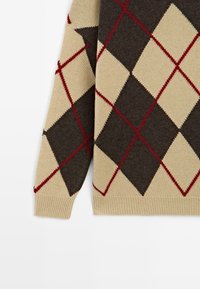 Pull en tricot avec un motif argyle en beige, marron et rouge. Détail de poignet côtelé, avec une texture douce et une coupe décontractée.