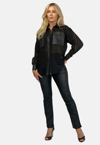 Czarna przezroczysta koszula zapinana na guziki z skórzanymi akcentami i dwiema przednimi kieszeniami, w zestawie z czarnymi dopasowanymi spodniami i szpilkami.