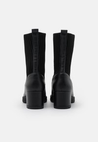 Mustat nilkkakorkokengät, joissa on ribbed-kangaspinta, sileä nahkapohja ja vetoketju takana. Korotettu lohkokorko.