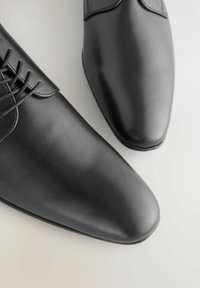 Fekete bőr dresszcipők sima felülettel, hegyes orrformával és fűzős záródással, finom varrási részletekkel.