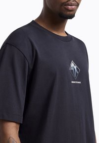 Zwart katoenen T-shirt met een diamantvormig logo met "AX" en "ARMANI EXCHANGE" in zilver. Korte mouwen en een relaxte pasvorm.