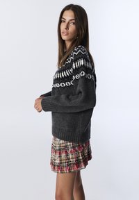 Maglione grigio a maglia con un giogo a motivo bianco e nero, abbinato a una mini gonna plissettata a quadri nei toni del rosso, giallo e verde.