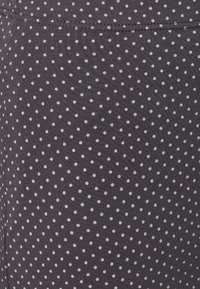 Tissu gris foncé avec un petit motif à pois blancs, présentant une texture lisse et des détails côtelés sur le bord supérieur.