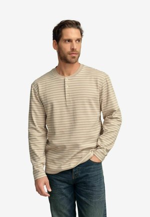 Beige långärmad henley-skjorta med horisontella ränder, med en knappslå och ribbad krage. Kombinerad med mörka jeans.