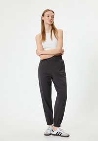 Schwarze Jogginghosen mit einem gerüschten Bund und elastischen Bündchen, kombiniert mit einem weißen gerippten Tanktop und weißen Sneakern mit schwarzen Streifen.