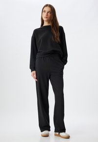 Schwarzer Sweatshirt und passende Hose aus weichem Stoff, mit lockerer Passform, elastischem Bund und einfachen weißen Sneakers.