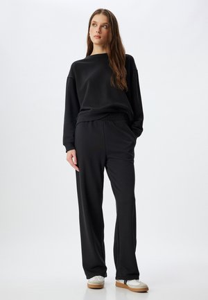 Schwarzer Sweatshirt und passende Hose aus weichem Stoff, mit lockerer Passform, elastischem Bund und einfachen weißen Sneakers.