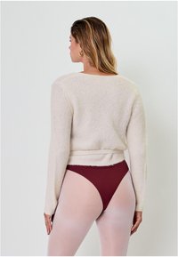 Kreemivärviline, kerge pikkade varrukatega sviiter, millel on vabalt langetatud lõige ning mis on kinnitatud vöökohal. Kandmine maroonide kõrge lõikega bikiinipükstega ja läbipaistvate sukkpükstega.