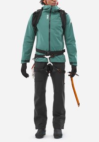 Person wearing teal jacket, black climbing harness and pants, black gloves, black hiking boots, and holding an orange ice axe.