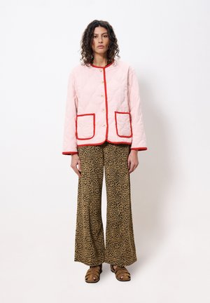 Veste rose matelassée avec des bordures rouges et des poches, associée à un pantalon large à imprimé léopard et des sandales à enfiler marron.