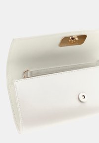 Interior de un bolso de cuero blanco con textura suave, herrajes dorados, cierre magnético y un bolsillo deslizable. Diseño simple y elegante.