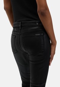 Czarne dżinsy z denimu o dopasowanym kroju; posiadają tylne kieszenie, delikatne przeszycia i gładką fakturę. Pas w talii ozdobiony jest małym logo.