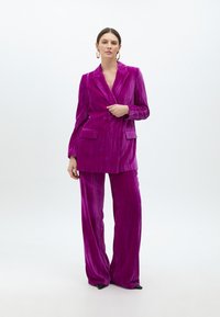 Lila sammetssuit bestående av en lång kavaj med snedskurna slag och dubbla knappar, i kombination med vida byxor, slät textur.