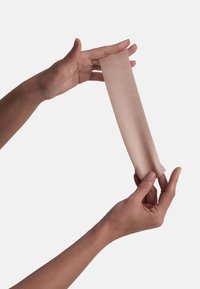 Nude elastinen kankaan palanen, jota pidetään kahden käden välissä, esittelee sileän pinnan ja hienovaraisen kiillon, pituus noin 20 cm ja leveys noin 5 cm.