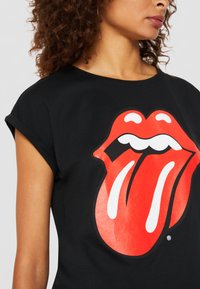 Sort bomulds T-shirt med et stort rødt og hvidt tunger grafik på fronten. Opsmøgede ærmer og en afslappet pasform.