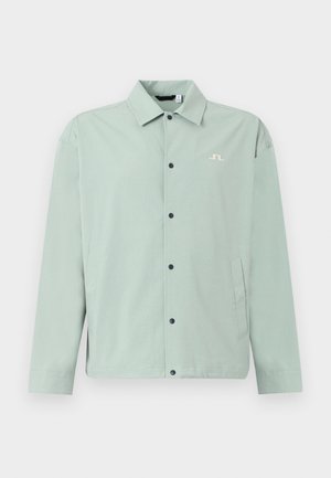 Hellgrüne Freizeitjacke mit Kragen, schwarzen Druckknöpfen vorne, Seitentaschen und einem kleinen weißen Sticklogo auf der Brust.