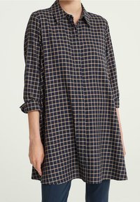 Marinblå skjorta med knappar och ett rutmönster i beige. Har krage och uppkavlade ärmar. Mjuk tyg med en ledig passform.