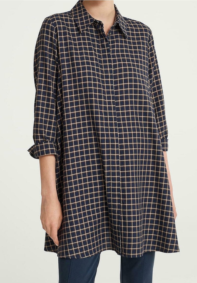 Marinblå skjorta med knappar och ett rutmönster i beige. Har krage och uppkavlade ärmar. Mjuk tyg med en ledig passform.