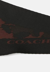 Czarna tkanina z haftowanym brzegiem i ciemnoczerwonym wzorem, częściowo ukazującym słowo "COACH" napisane dużymi literami.